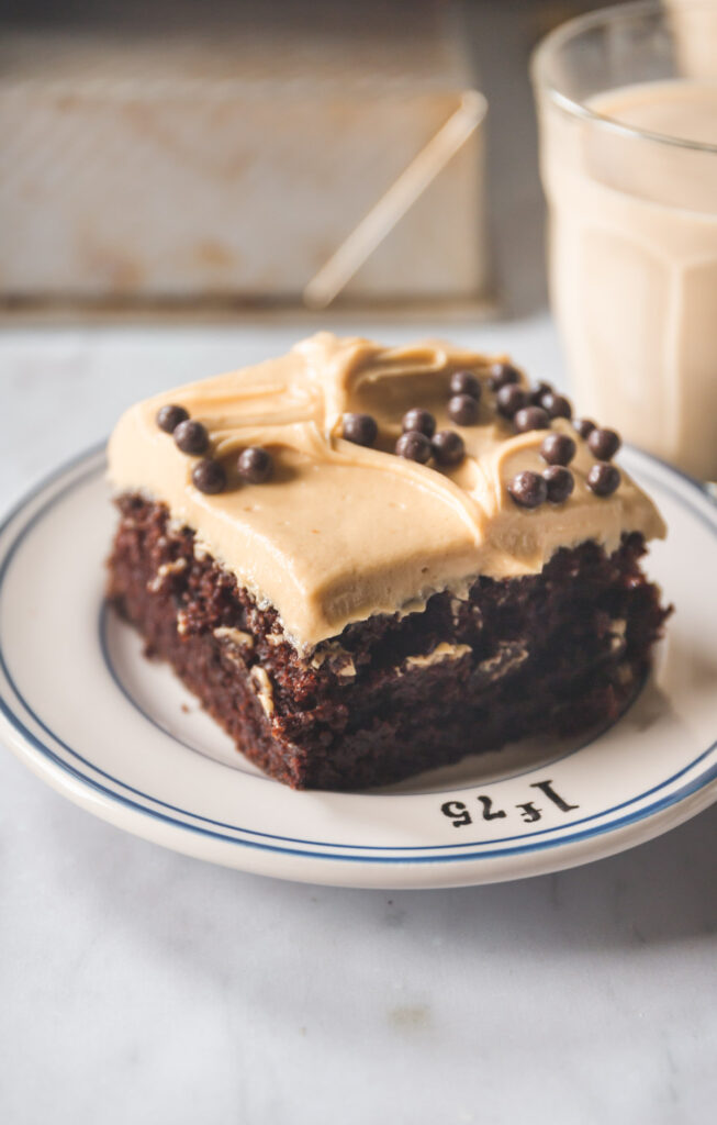 A square slice of A chocolate sheet cake with peanut butter frosting topped with chocolate crunch balls on a small white plate with blue stripes