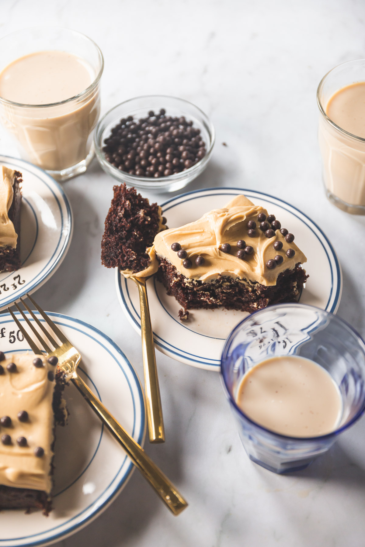 A square slice of A chocolate sheet cake with peanut butter frosting topped with chocolate crunch balls on a small white plate with blue stripes