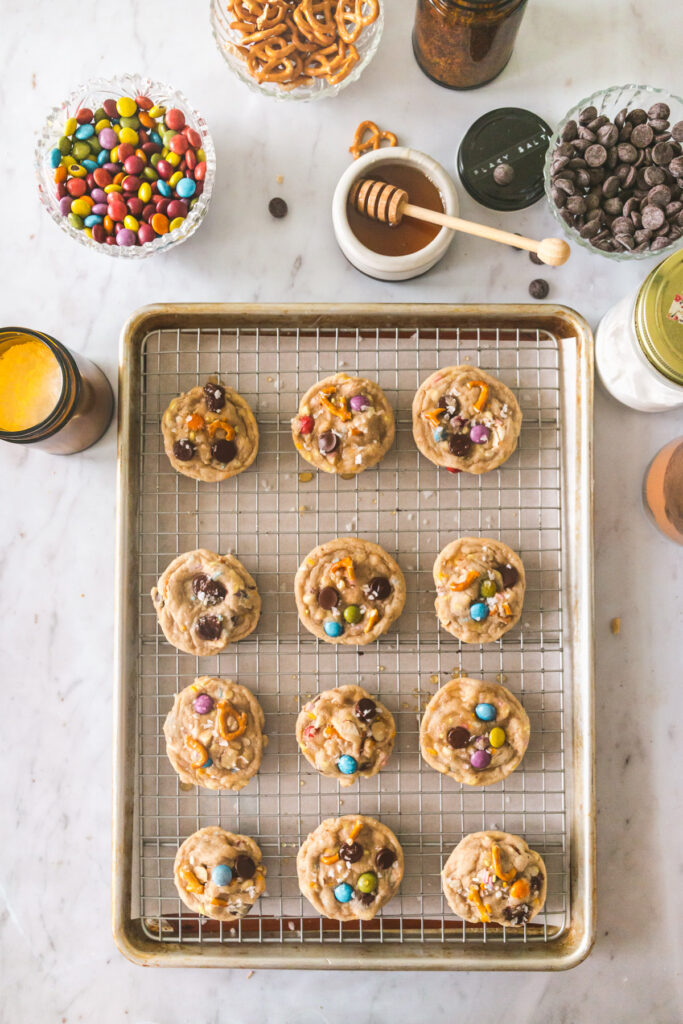 Kitchen Sink Cookies on a cooling rack with honey and toppings in the background