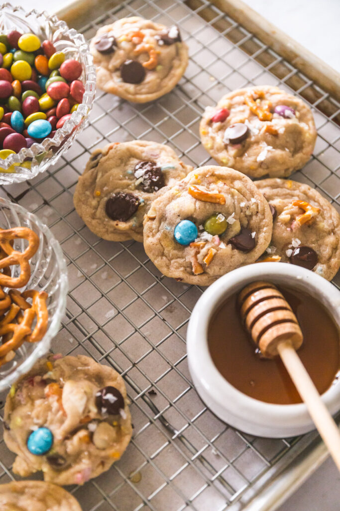 Overhead image of Kitchen Sink Cookies on a cooling rack with honey, pretzels, m&ms