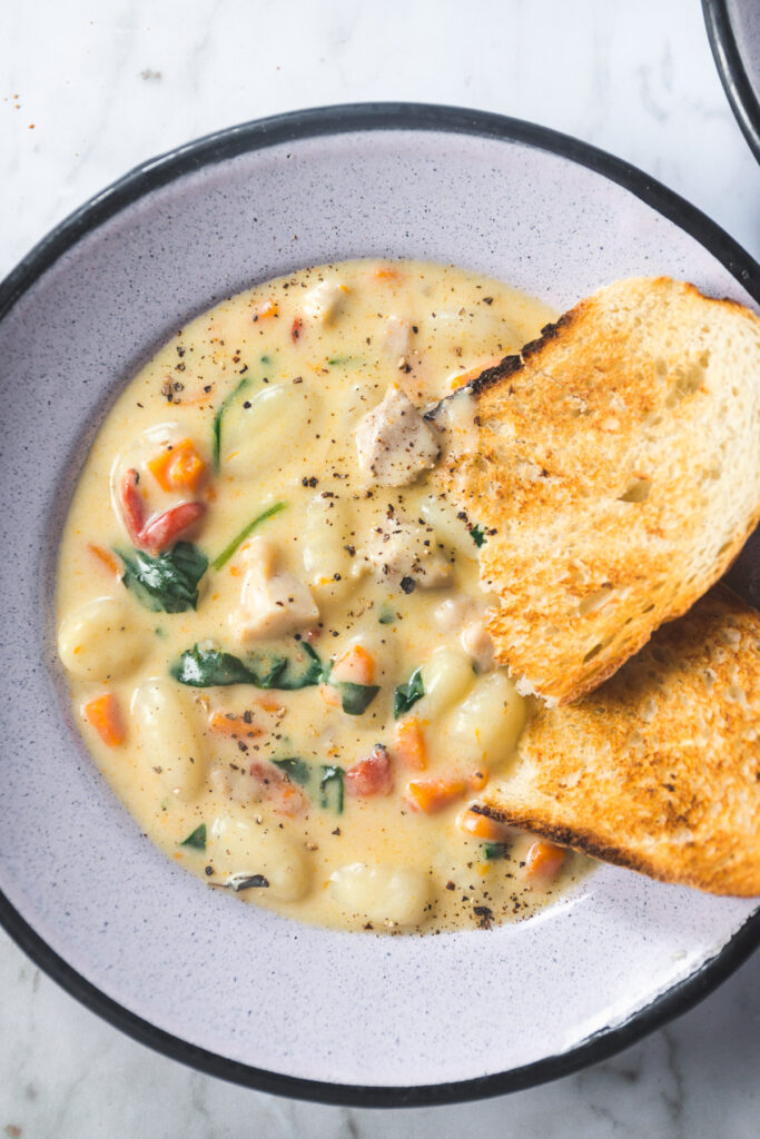 Overhead shot of Creamy Chicken Gnocchi Soup with crusty bread dipped in