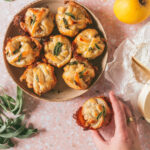 overhead shot of a bowl of Apple Chanterelle Brie Stuffed Pastry with one hand holding a sinlge Apple Chanterelle Brie Stuffed Pastry