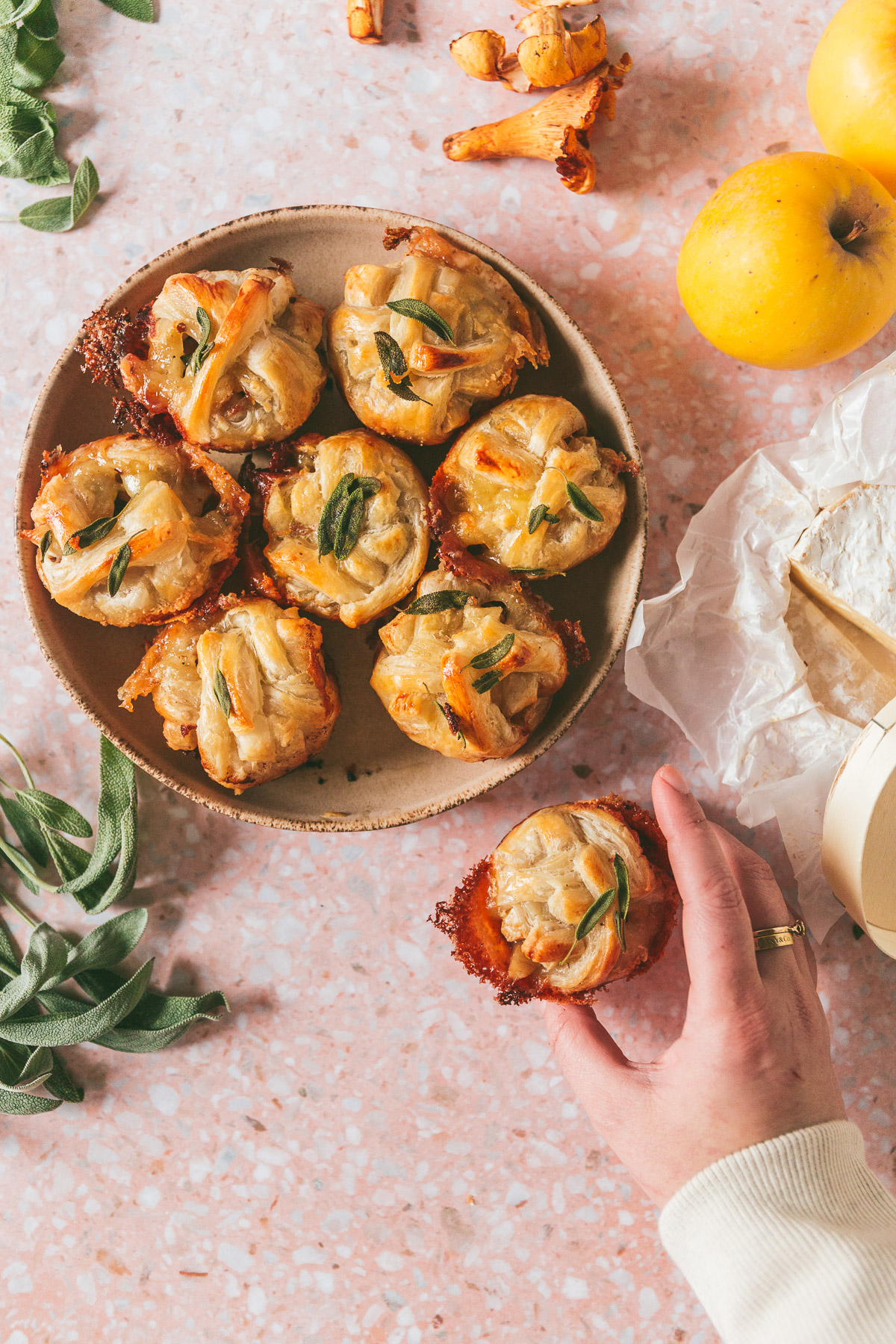 overhead shot of a bowl of Apple Chanterelle Brie Stuffed Pastry with one hand holding a sinlge Apple Chanterelle Brie Stuffed Pastry