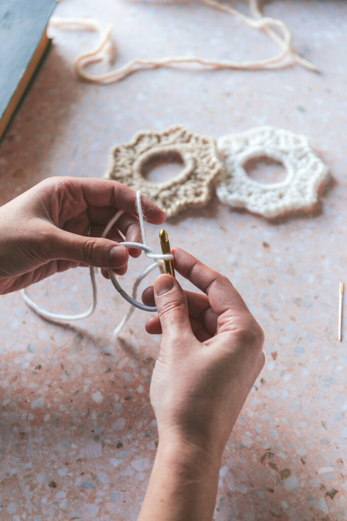 Hands kitting the knit scrunchie with cream and white yarn