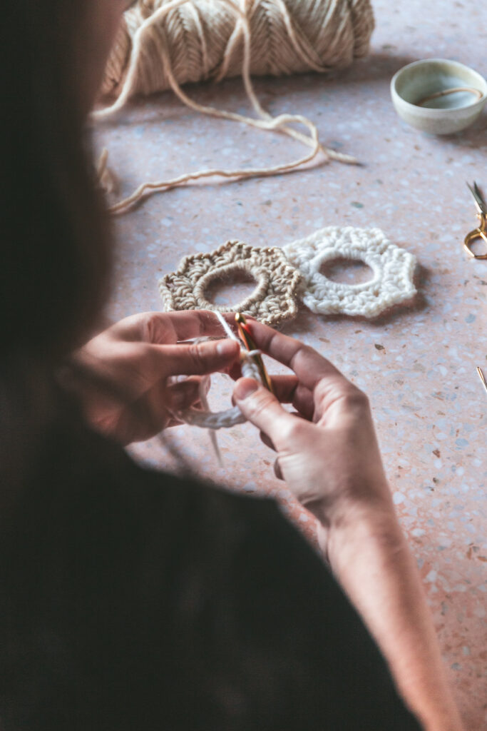 Hands kitting the knit scrunchie with cream and white yarn