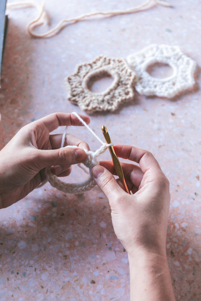 Hands kitting the knit scrunchie with cream and white yarn