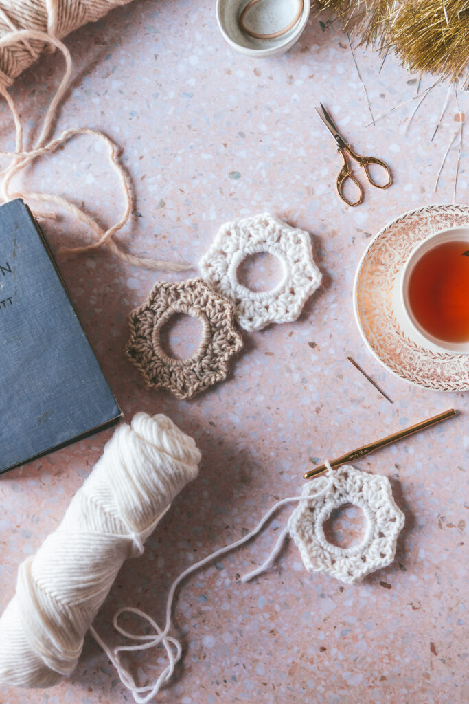 Overhead of two scrunchies on a pink background and a cup of tea on the side with all the knitting elements